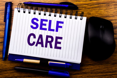 Handwritten text showing Self Care. Business concept for Taking caring for own Health written on notebook book note paper on wooden background. Blue word letters. Next to mouse.