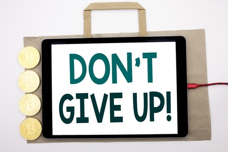 Handwritten text showing Don t Give Up. Business concept writing for Motivation Determination, Written on shopping bag and tablet white background, tablet charging with cryptocurrency bitcoin.の写真素材