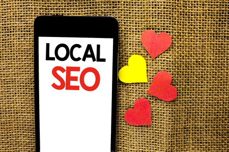 Text sign showing Local Seo. Conceptual photo Search Engine Optimization Strategy Optimize Local Find Keywords written Cardboard Piece Holding By Sculpture the jute background.の写真素材