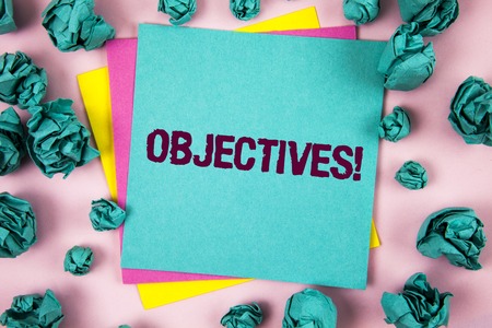 Handwriting text Objectives Motivational Call. Concept meaning Goals planned to be achieved Desired targets written Sticky Note Paper plain background Crumpled Paper Balls next to it.の写真素材