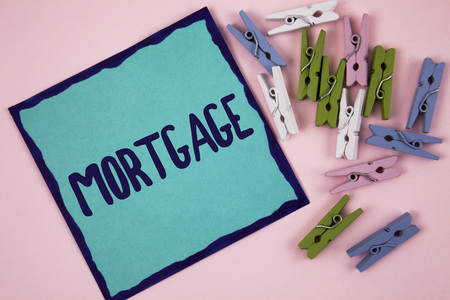 Handwriting text writing Mortgage. Concept meaning Conditional right of property to lender as warranty from loan written Sticky note paper plain Pink background Wooden Clips next to it.の写真素材
