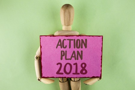 Handwriting text writing Action Plan 2018. Concept meaning to do list in new year New year resolution goals Targets written Sticky note paper holding by Wooden Robot Toy on plain background.の写真素材