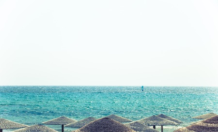 Beach view with straw umbrellas. Beautiful blue calm water clear sky landscape. Summer vacation time. Relaxation. Luxury destination. Traveling abroadの写真素材