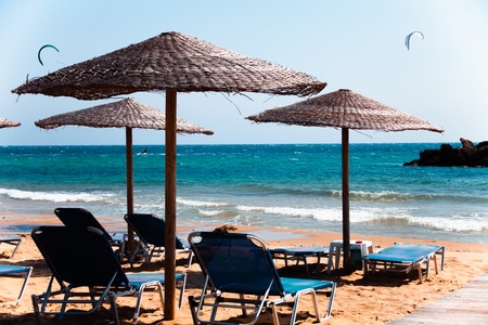 Lounge Chairs under Straw Umbrellas on beautiful sandy beach in Corfu Greece. Seashore great view. Transparent turquoise water. Summer vacation time. Relaxation in chair and umbrellaの写真素材