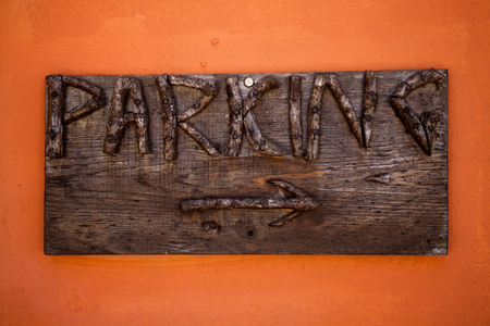 Parking sign. Rustic wooden boards with engraved letters and arrow in orange wall. Indication to public space to park vehicles. Directions. Carved wood signsの写真素材