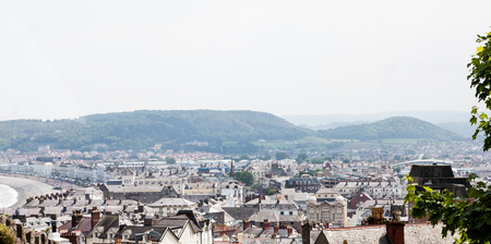 City of Llandudno in North Wales, United Kingdom. Traditional UK cityscape from the hilltop. Town aerial view over busy main street and houses. Photo of british houses' roofs and chimneysの写真素材