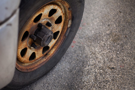 A closeup view of a heavily used car tyre that seems abandoned a longtime ago. There are also rusted rim hubcap and  screws that badly needs maintenance.の写真素材