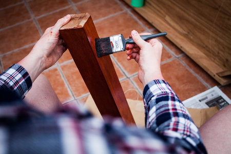 Man holds painting brush and paints wooden board. Closeup view of home renovating and old furniture painting.  Top view of hands holding painting brushの写真素材