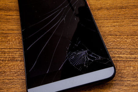 Crashed mobile phone on the table. Black mobile phone on the wooden table with crashed lcd display....
