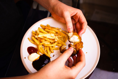 Man is holding chicken fried wings in his hands. Eating meat with hands. Delicious meal prepared with french fries. Unhealthy eating conceptの写真素材