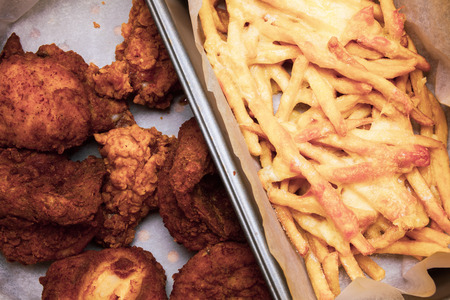 Flat lay above table with fried chicken wings and french fries in the box. Served unhealthy meal. Fast food meal served in the paper box. Delicious mouth watering food.の写真素材