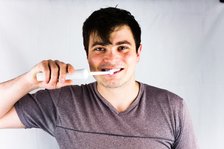 Close-up of young man brushing teeth with electric toothbrush. Joyful young man smiling during morning teeth brushing. Health and beauty concept image with brushing teethの写真素材