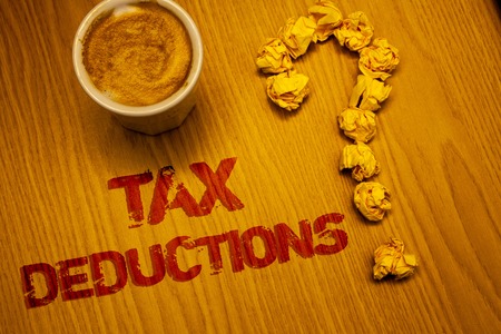 Text sign showing Tax Deductions. Conceptual photo Reduction on taxes Investment Savings Money Returns Words written Desk Coffee White mug crumbled paper notes question markの写真素材
