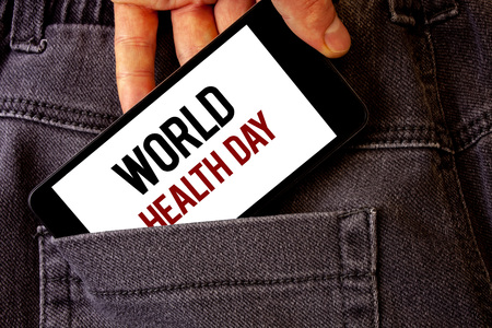 Conceptual hand writing showing World Health Day. Business photo showcasing Special Date for Healthy Activities Care Prevention Man holding cell phone white screen letters jeans pocketの写真素材