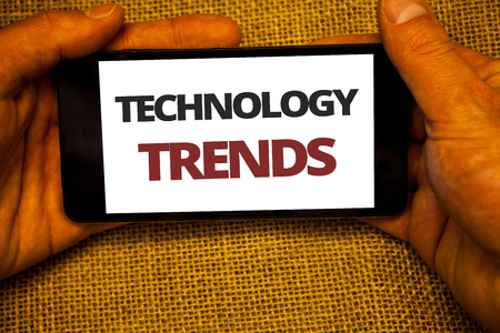 Text sign showing Technology Trends. Conceptual photo Trending Modern Viral Advanced Development Trendy New Jute sack background hand holding iPhone with colorful alphabetic syllableの写真素材