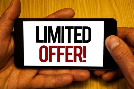 Text sign showing Limited Offer Motivational Call. Conceptual photo Short time special clearance Price Reduction Two hands holding black phone screen words written home button pressの写真素材