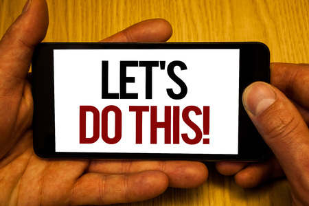 Text sign showing Let Us Do This Motivational Call. Conceptual photo Encourage to start something Inspirational Two hands holding black phone screen words written home button pressの写真素材