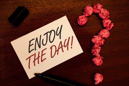 Text sign showing Enjoy The Day Motivational Call. Conceptual photo Enjoyment Happy Lifestyle Relaxing Time Text white paper note black marker open cap pink crumbled paper questionの写真素材