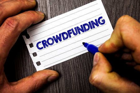 Writing note showing  Crowdfunding. Business photo showcasing Funding a project by raising money from large number of people Man hold holding marker notebook paper ideas wood wooden backgroundの写真素材