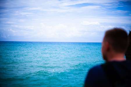 Man sitting on the cliff. Tourist ovelooking the sea. Waves shoaling and approcahing the seabed. Relaxing tropical destination. Sightseeing and outdoor unwinding activity.の写真素材