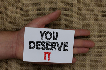 Writing note showing You Deserve It. Business photo showcasing Reward for something well done Deserve Recognition award Human hand holding white page with black and red color texts on sackの写真素材