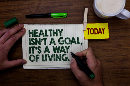 Word writing text Healthy Isn t not A Goal, It s is A Way Of Living.. Business concept for Create good habits routines Man holding marker notebook clothespin reminder wooden table cup coffeeの写真素材
