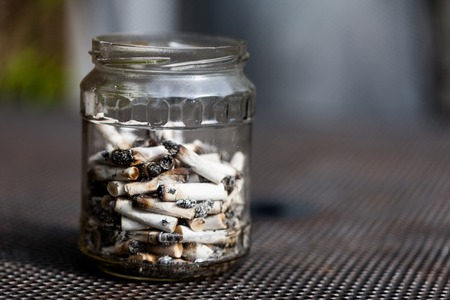 Jar full with smoked cigarette filters. Pile of dirty smoked cigarette filters in the glass bowlの写真素材