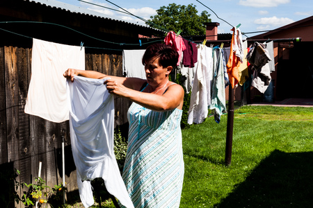 American woman looking serious on the garment to be hang for sun dry. Pants shirts and other clothes hanging on the metal string outside the house. Household chore of a typical housewifeの写真素材