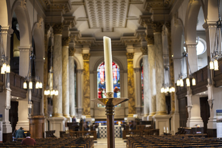 BIRMINGHAM, UK - March 2018 One Used White Candle Standing in the Middle Foregroound. St. Philips Cathedral Interior Serving as Blur Background. Few People Inside the Church Prayingのeditorial素材