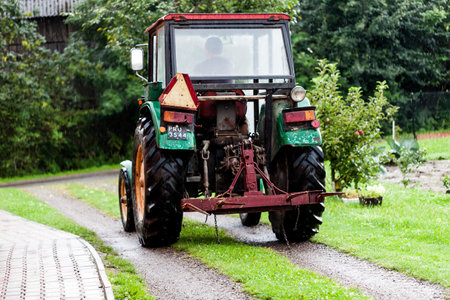Four Wheeled Drive Mini Truck Hay Reaper in the Farm with Driver. Trees and Fruit Bearing Plants in the Area. Drizzle Makes the Grass More Fresh and Greenのeditorial素材