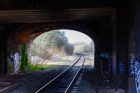 BIRMINGHAM, UK - March 2018 Railway Track under Bridge Decayed Underground. Gravel and Dry Twigs Around the Area. Vandalism on the Dirty Bricked Wall. Fresh Leaves Crawl up the Wallのeditorial素材