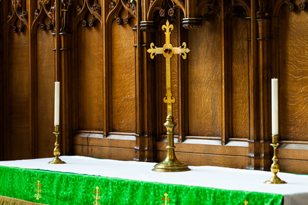 BIRMINGHAM, UK - March 2018 Celtic Cross and Candlestick Holder Made of Brass Standing on Altar Counter. Elaborate Wood Carving Details on Wall Panel. Santuary Linen Covers the Tableのeditorial素材