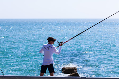 Brighton, UK - June 2018 Man with Cap Standing Ashore Holding Long Fishing Rod with Reel. Crystal...