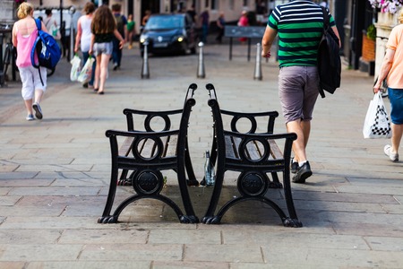 BIRMINGHAM, UK - March 2018 Two Iron Metal Bench in Public Commercial Area Facing Opposite Side. People Walking in One Way Direction. Individual Steel Barrier Standing at the Far Endのeditorial素材