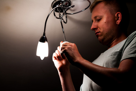 A middle-aged man changes the bulb on the ceiling. A man installs a new light bulb on the ceilingの写真素材