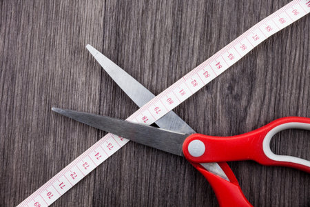 Front view wooden background scissors cutting through tape measuring dietの写真素材