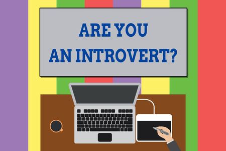 Text sign showing Are You An Introvert question. Business photo text demonstrating who tends to turn inward mentally Upper view laptop wooden desk worker drawing tablet coffee cup officeの写真素材