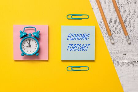 Conceptual hand writing showing Economic Forecast. Concept meaning Process of making predictions about the economy condition Notepads colored paper sheet markers alarm clock wooden backgroundの写真素材
