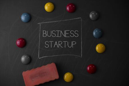 Text sign showing Business Startup. Business photo text Putting up new commerce venture Fresh Undertaking Round Flat shape stones with one eraser stick to old chalk black boardの写真素材
