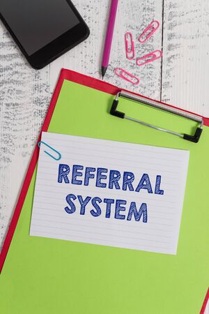 Writing note showing Referral System. Business concept for sending own patient to another physician for treatment Clipboard sheet pencil smartphone squared note clips wooden backgroundの写真素材