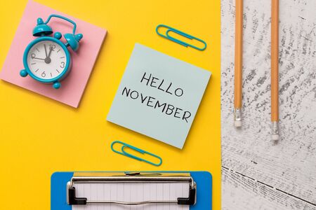 Writing note showing Hello November. Business concept for Welcome the eleventh month of the year Month before December Notepads paper sheet clipboard markers alarm clock wooden backgroundの写真素材