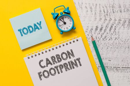 Text sign showing Carbon Footprint. Business photo showcasing amount of dioxide released atmosphere result of activities Spiral notepad paper sheet marker alarm clock retro wooden backgroundの写真素材