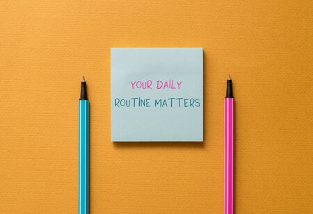 Text sign showing Your Daily Routine Matters. Business photo showcasing practice of regularly doing things in fixed order Front view blank colored sticky note two ballpoints cool yolk backgroundの写真素材