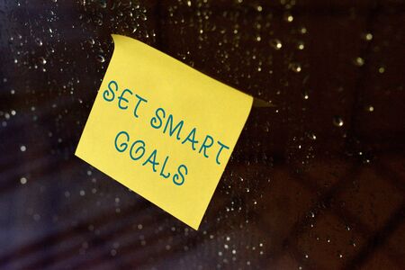 Conceptual hand writing showing Set Smart Goals. Concept meaning giving criteria to guide in the setting of objectives Square paper piece notation stick to textured glass windowの写真素材