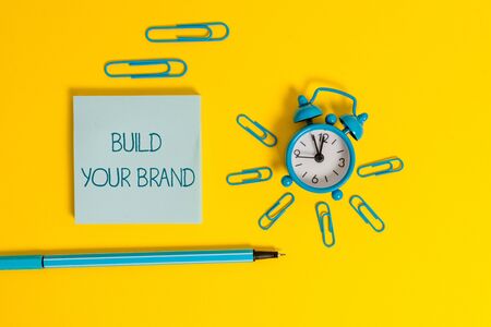 Word writing text Build Your Brand. Business photo showcasing enhancing brand equity using advertising campaigns Metal alarm clock wakeup clips ballpoint notepad colored backgroundの写真素材