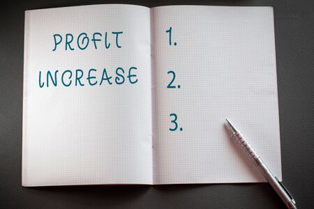 Word writing text Profit Increase. Business photo showcasing the growth in the amount of revenue gained from a business Checkered math book and classic silver pen placed above textured work deskの写真素材