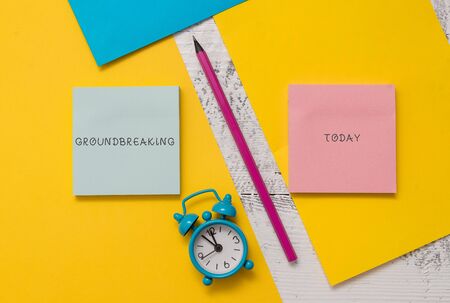 Text sign showing Groundbreaking. Business photo text Very new and a big change from other things of its type Notepads marker pen colored paper sheets alarm clock wooden backgroundの写真素材
