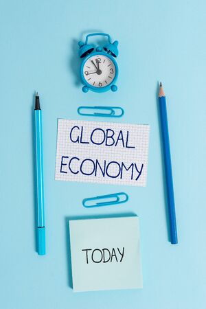 Writing note showing Global Economy. Business concept for System of industry and trade around the world Capitalism Alarm clock squared paper sheet notepad markers colored backgroundの写真素材