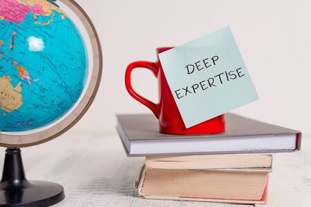Writing note showing Deep Expertise. Business concept for Great skill or broad knowledge in a particular field or hobby Globe map world earth cup blank sticky note stacked books wooden tableの写真素材