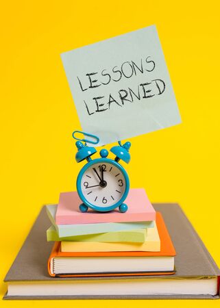 Handwriting text writing Lessons Learned. Conceptual photo the knowledge or understanding gained by experience Alarm clock note stacked notepads old books colored backgroundの写真素材